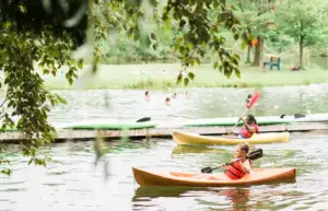 2 girls ride yellow kayaks by the dock on a peaceful lake.